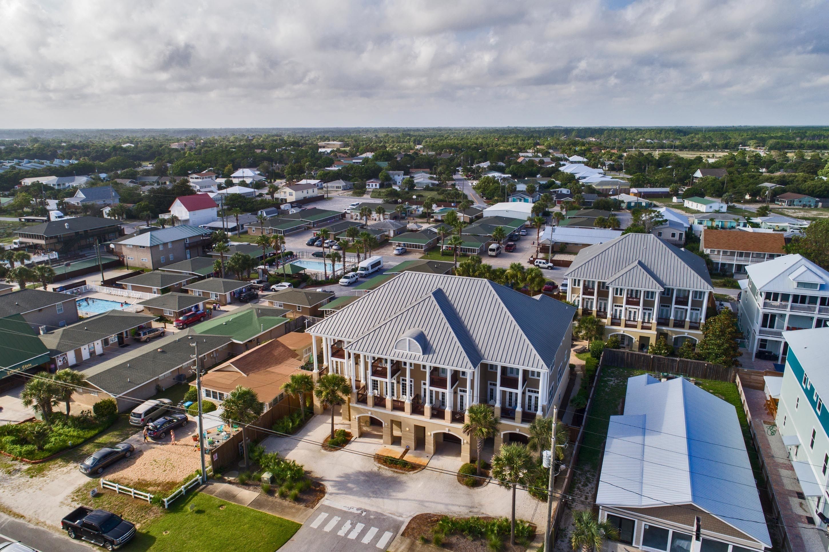 An aerial view of a residential area with houses, a large building with a sloped roof, and a swimming pool.