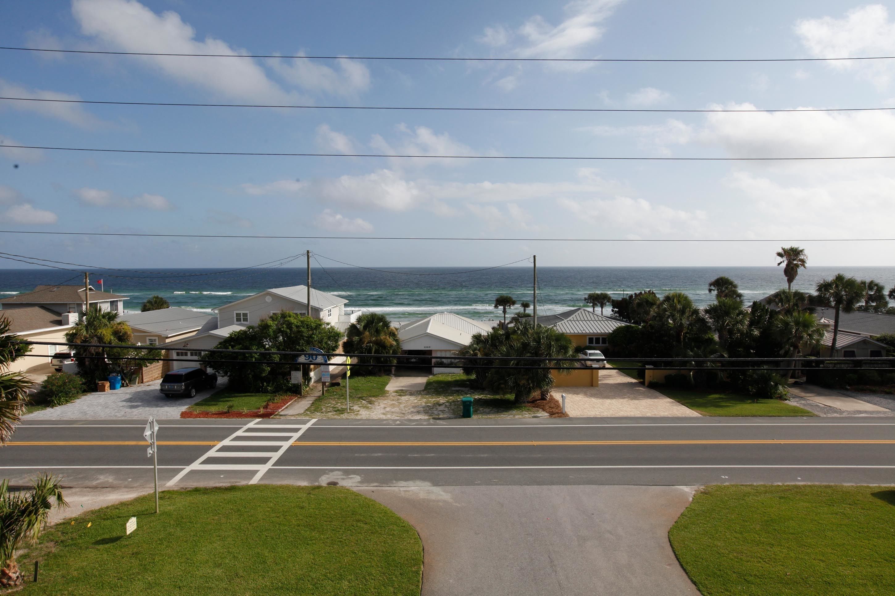 Eine Wohnstraße mit Häusern, blauem Himmel und dem Meer im Hintergrund.
