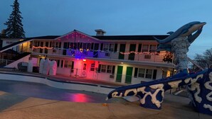 A building with a balcony decorated with lights and a large dolphin sculpture in the foreground. - Colonial Motel (Wisconsin Dells)