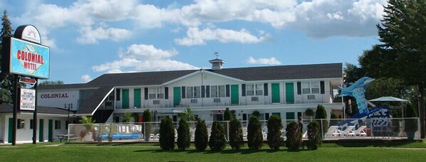 A Colonial Motel with a two-story structure, a fenced front yard, and a large blue sculpture.