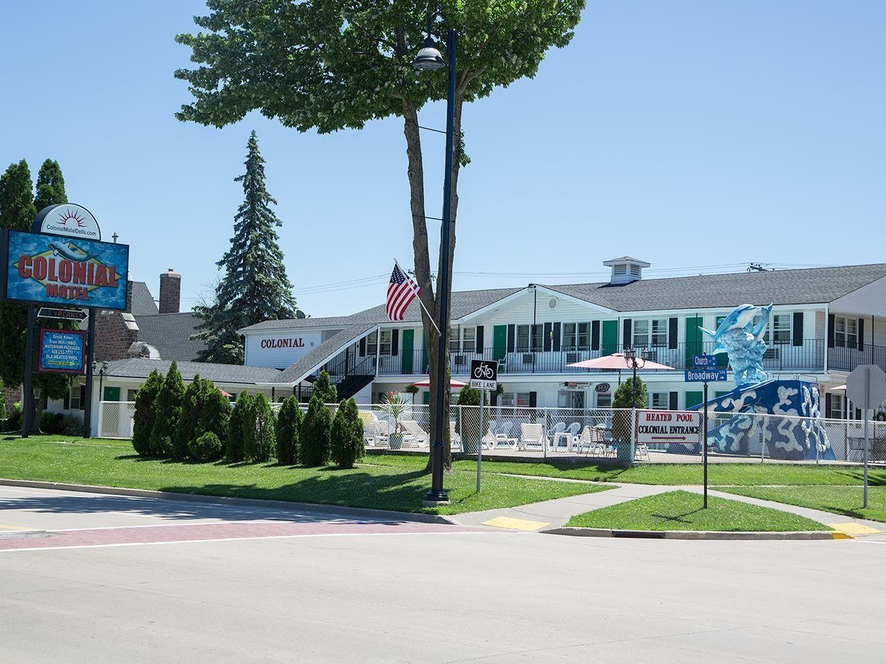 A Colonial Motel with a signboard, an American flag, a bike lane sign, and a heated pool entrance sign.