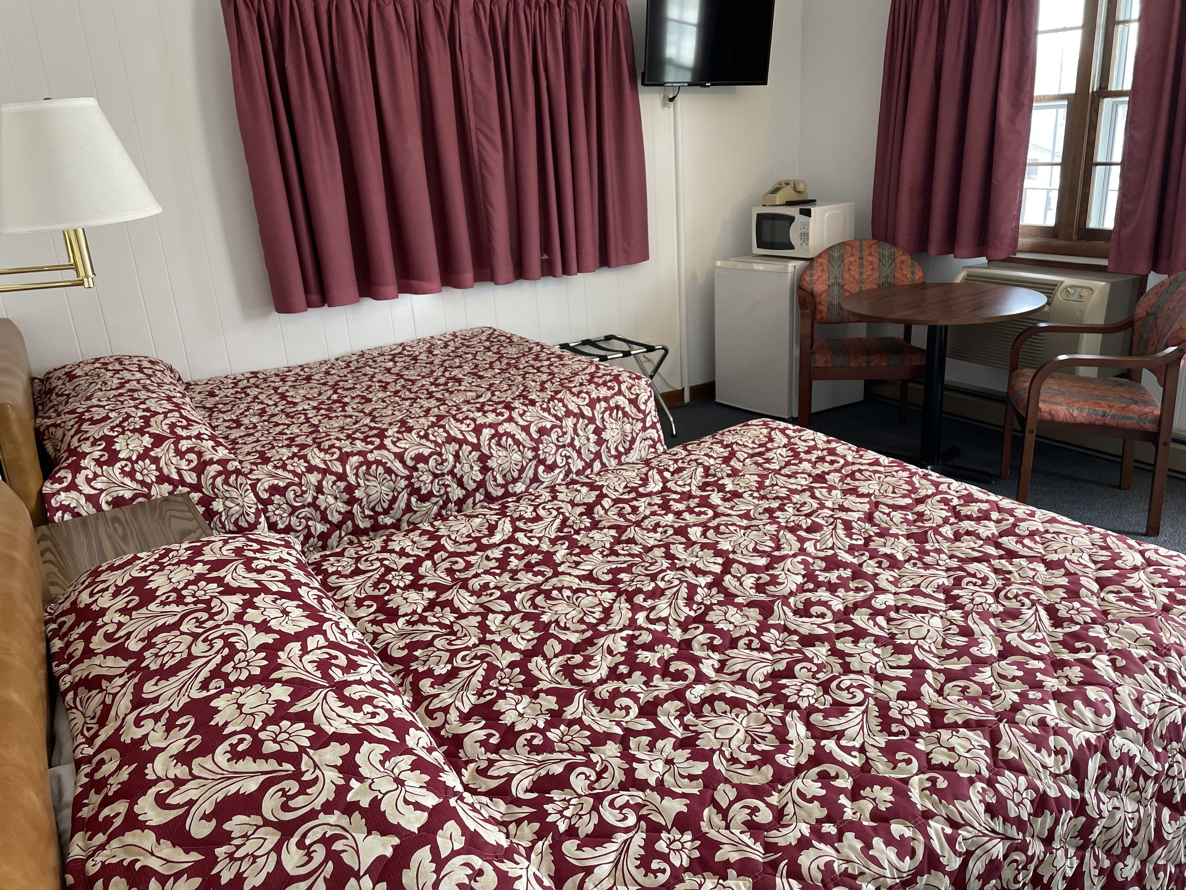 Een hotelkamer met twee bedden, een televisie, een magnetron, een stoel en een tafel.