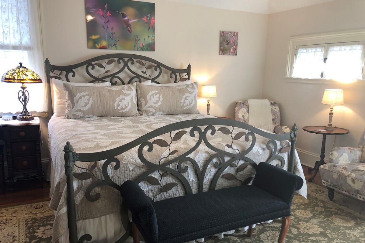 A bedroom with a bed, bedside tables, a bench, a chair, and artwork on the walls.