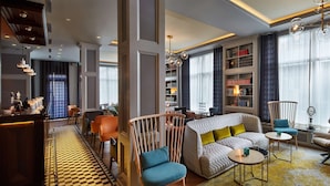A modern hotel lobby with a checkered floor, a bar area, seating arrangements, and large windows with curtains. - Reykjavik Konsulat Hotel, Curio Collection by Hilton (Reykjavik)