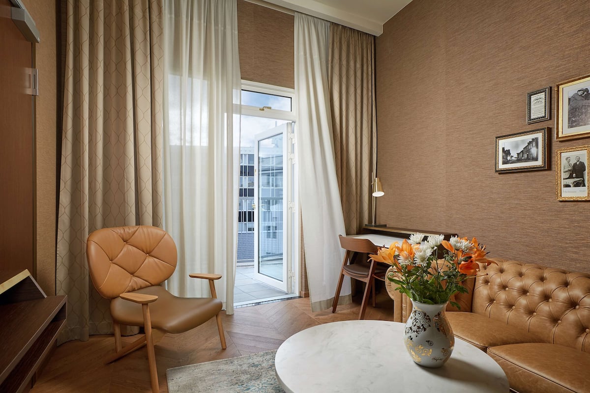 En moderne stue med en lædersofa, et spisebord og et stort vindue med gardiner.