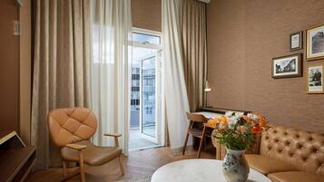 A modern living room with a leather sofa, a dining table, and a large window with curtains.