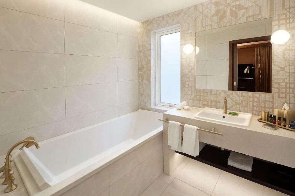 A modern bathroom with a bathtub, two sinks, a window, and a mirror.