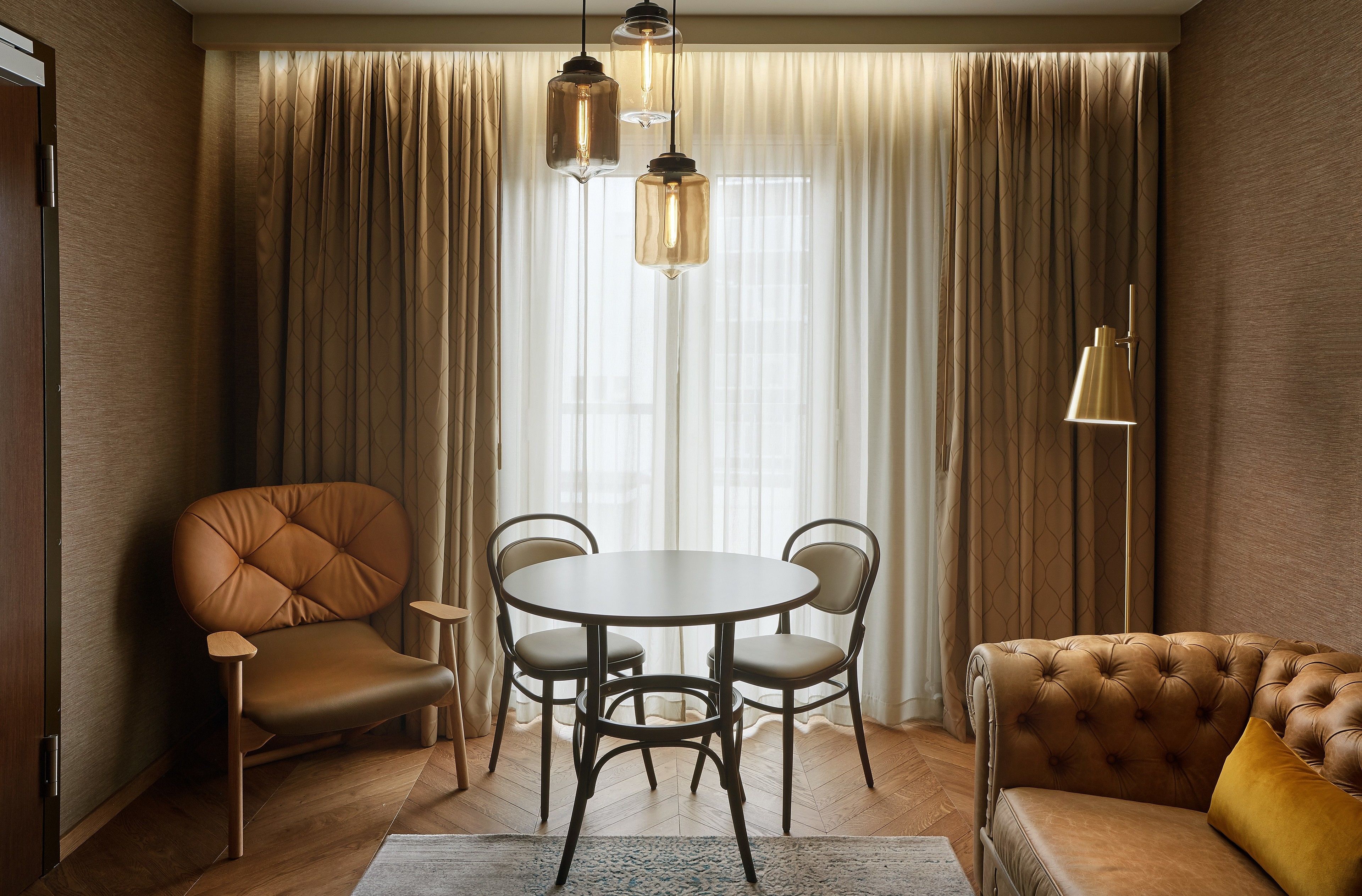 A room with a round table, two chairs, a sofa, and a floor lamp.