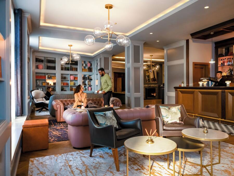 A modern lounge area with leather sofas, a bar, and a well-stocked bookshelf.