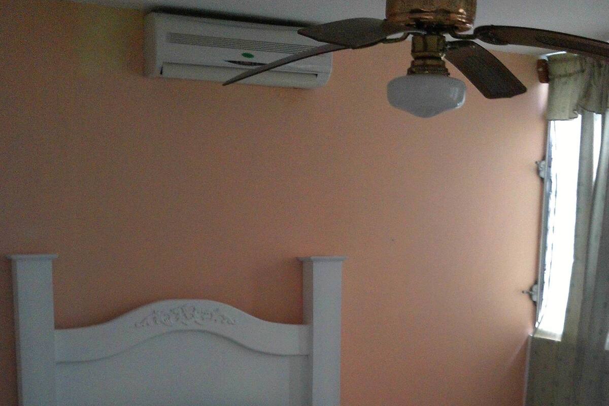 A neatly made bed with white linens and pillows, a white nightstand with a lamp, and a ceiling fan above.