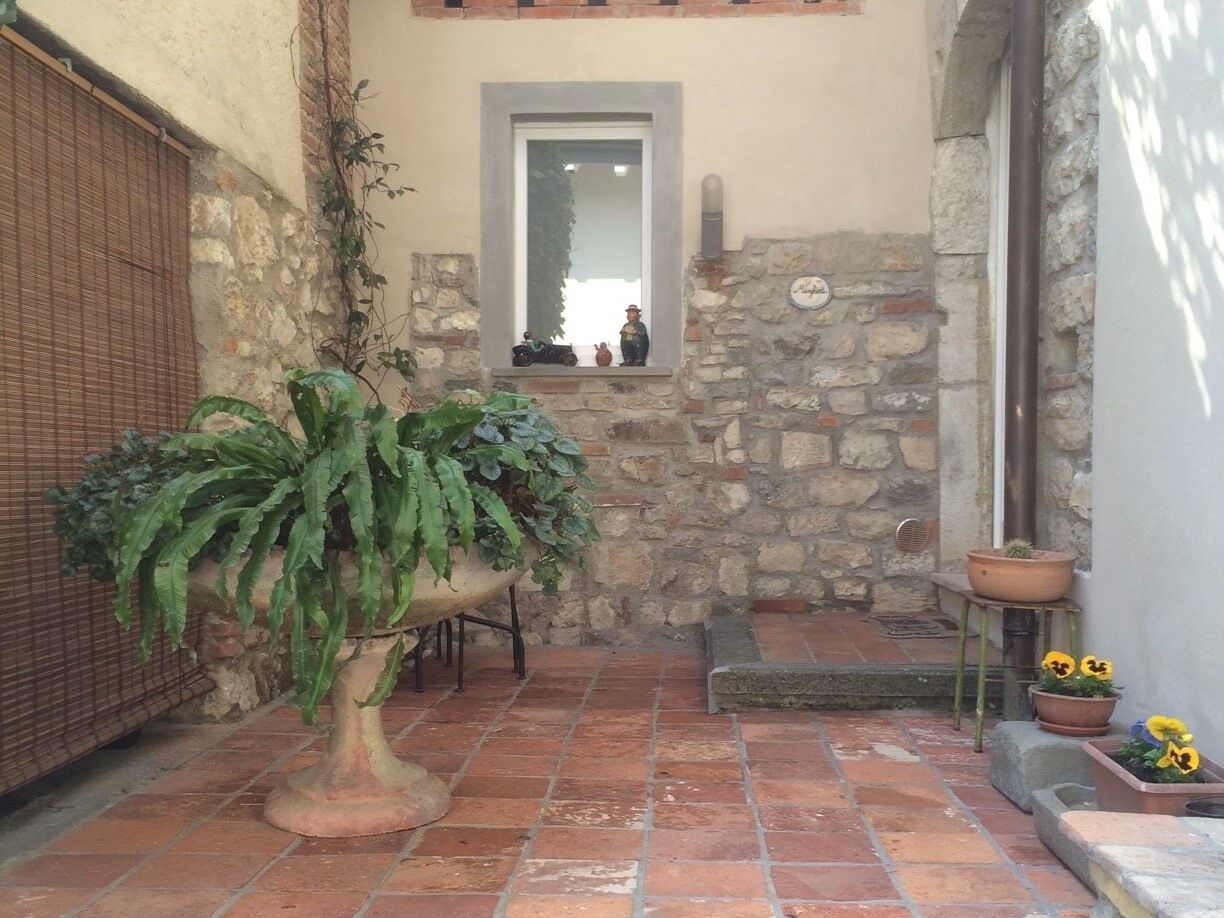 A stone-walled courtyard with a potted plant, a small window with a reflection, and a few flower pots.