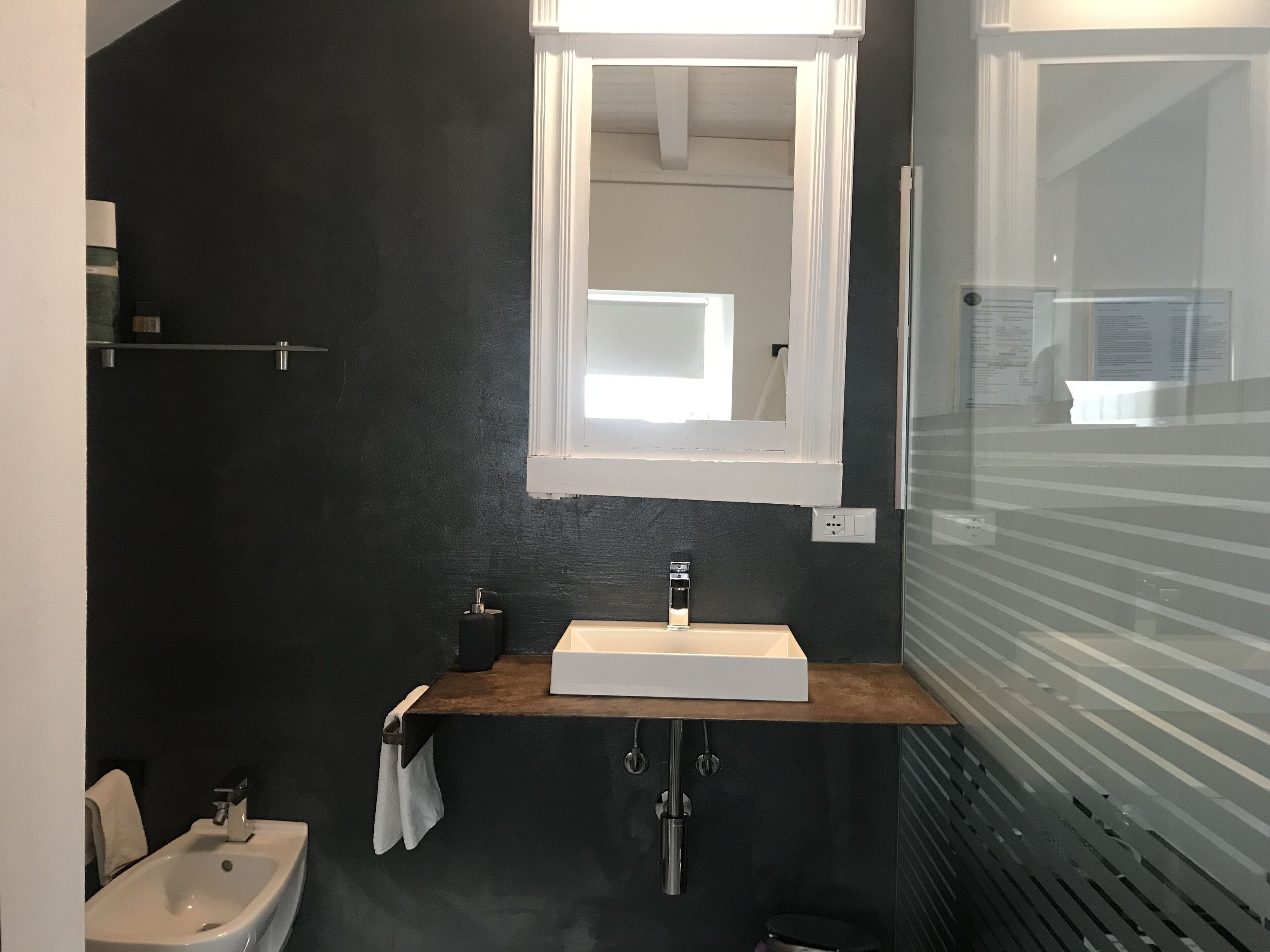 Un baño moderno con una pared oscura, un lavabo blanco, un espejo y una ventana.