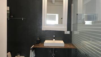 Un baño moderno con una pared oscura, un lavabo blanco, un espejo y una ventana.