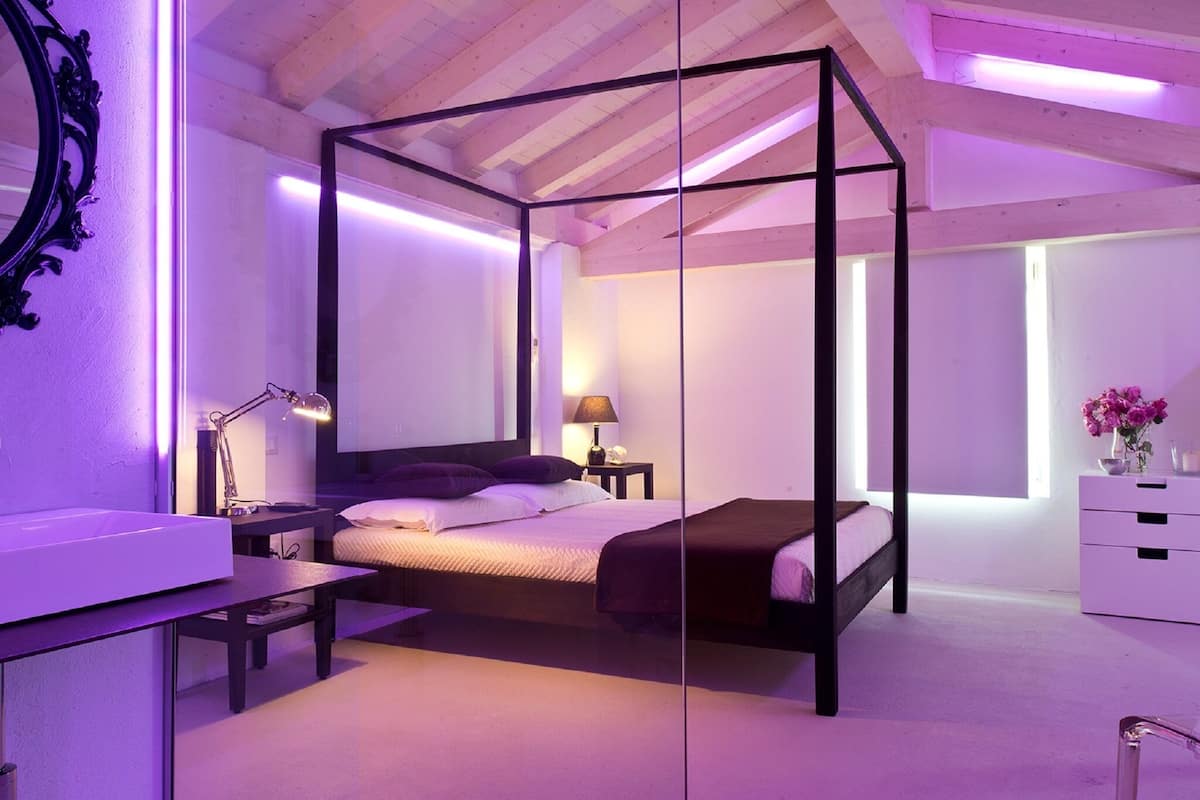 A modern bedroom with a four-poster bed, a desk with a lamp, and a dresser.