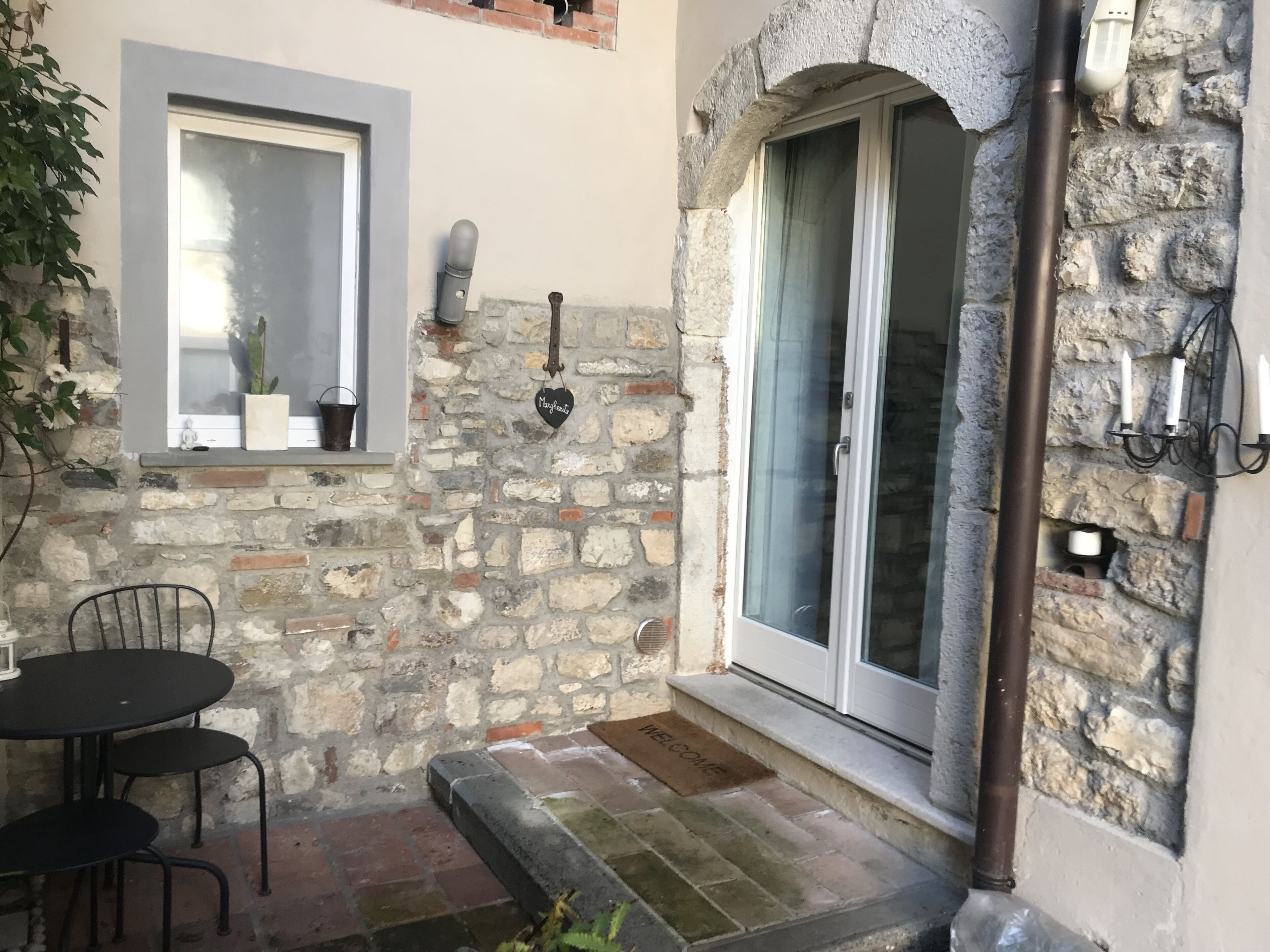 A stone exterior with a door, a window with a potted plant, and a small table with chairs.