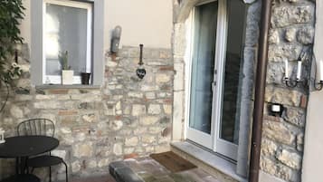 A stone exterior with a door, a window with a potted plant, and a small table with chairs.
