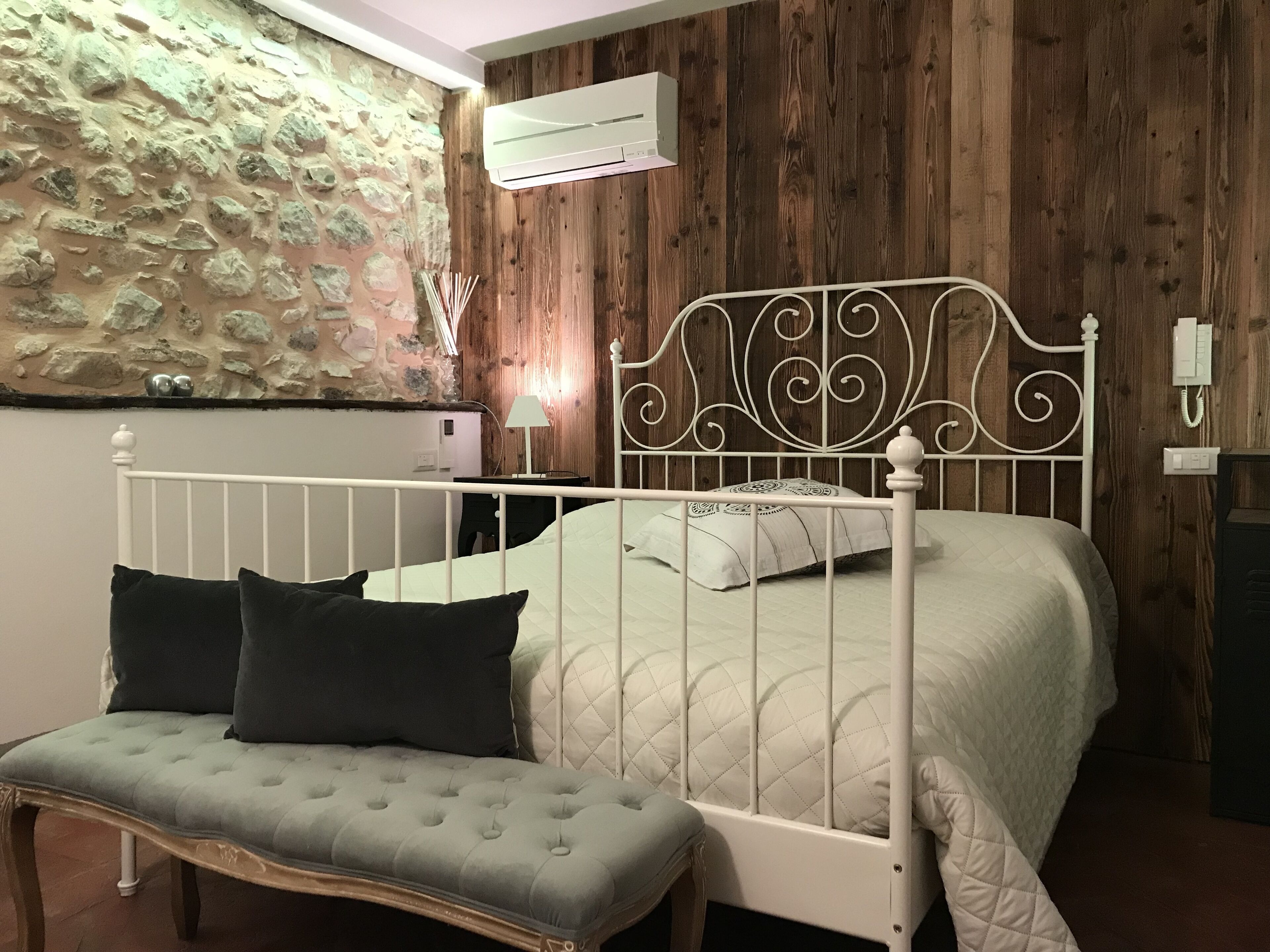 A bedroom with a bed, a bench, a wall-mounted air conditioner, and a wooden wall.