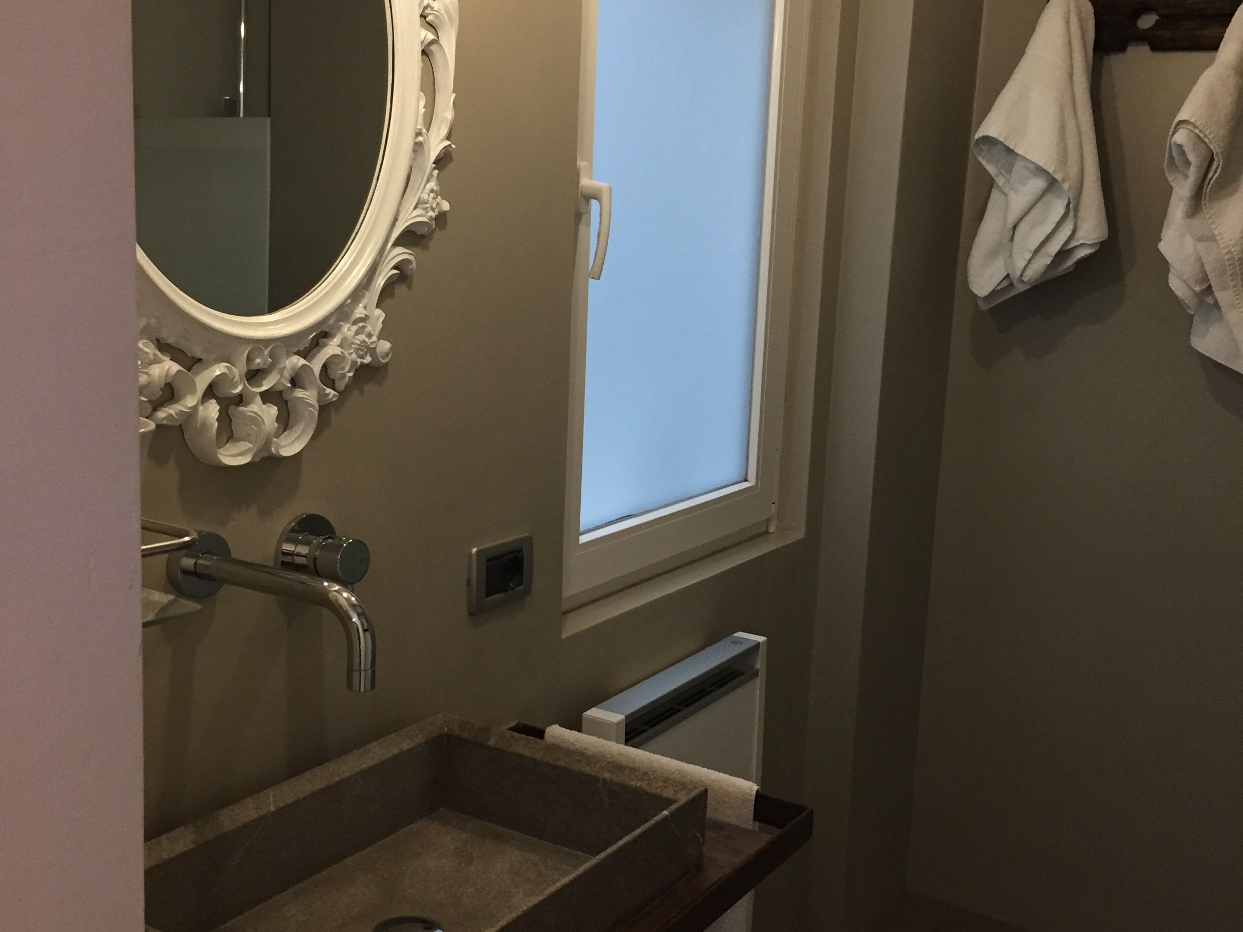 Ein Badezimmer mit großem Spiegel, Waschbecken, Fenster und Handtuchhalter.