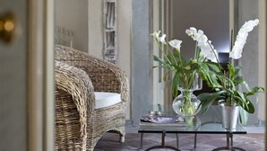 Un canapé en osier, une table en verre ornée d’un vase de fleurs blanches et une plante en pot.