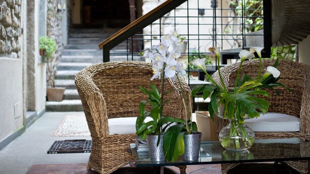 Un canapé en osier avec des coussins blancs, une table en verre ornée de plantes en pot et un escalier en arrière-plan.