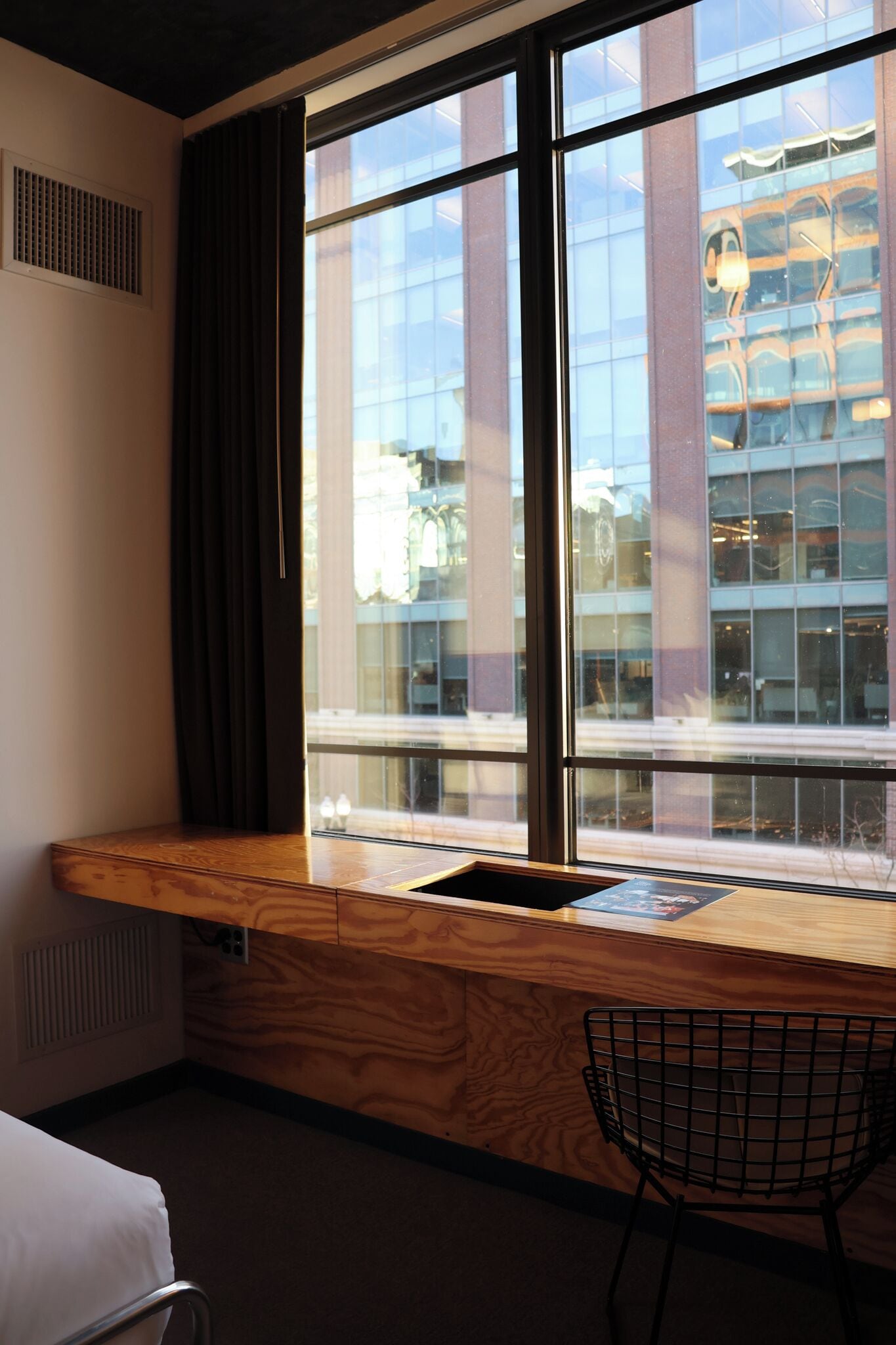 Hotellihuone, jossa on suuri ikkuna, puinen työpöytä, tuoli ja sänky.