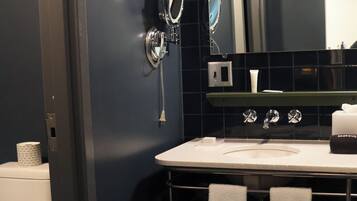 A modern bathroom with a dark blue tiled wall, a white sink, a mirror, and a hairdryer mounted on the wall.