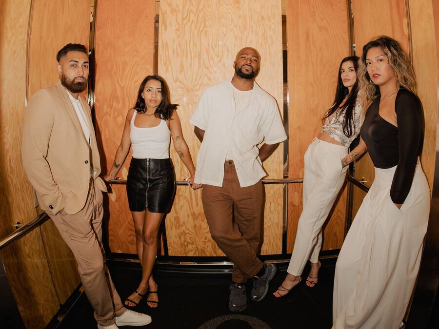 A group of people standing in an elevator with wooden walls and a metal door.
