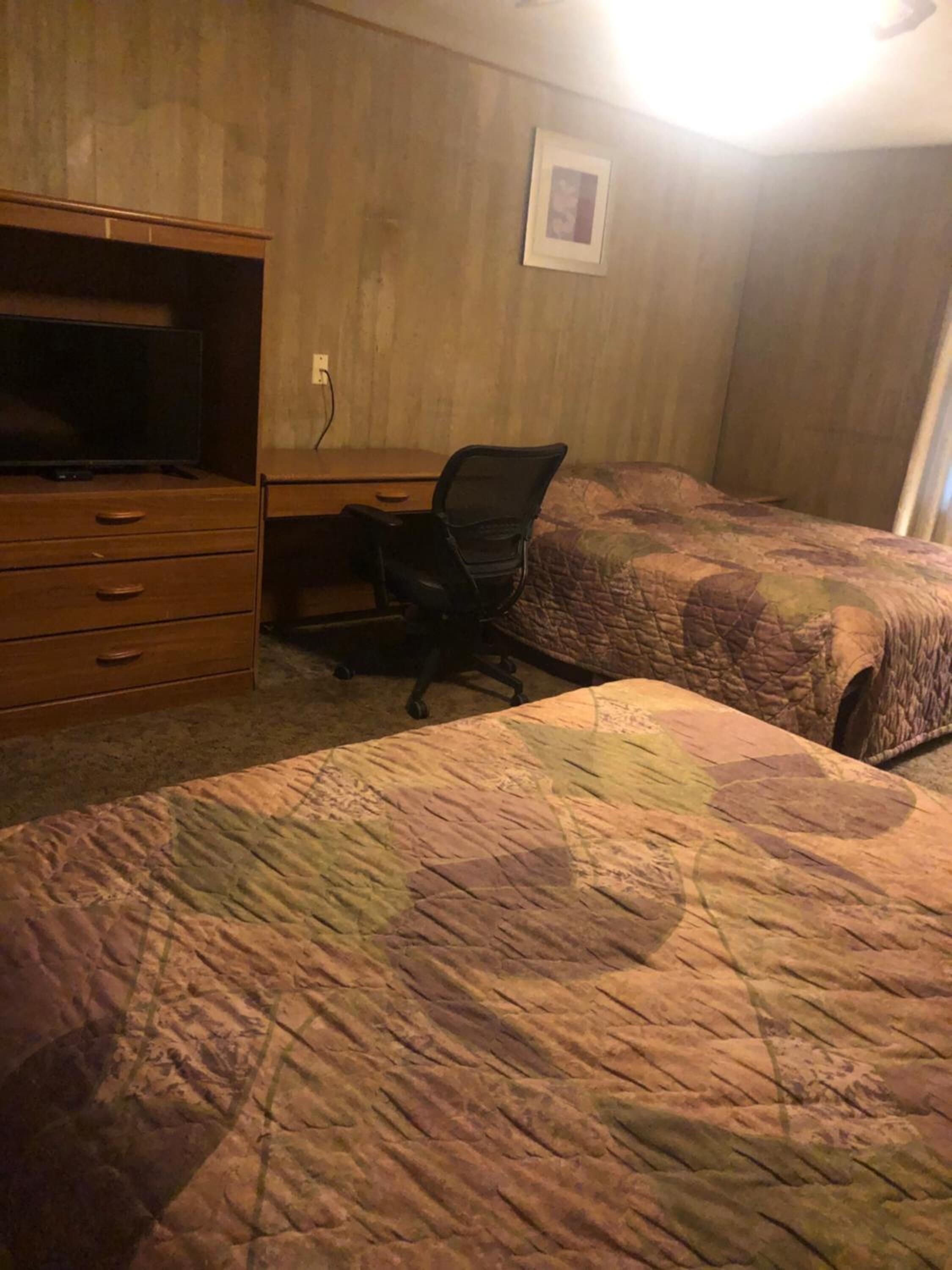 A bedroom with two beds, a desk, a chair, and a television.