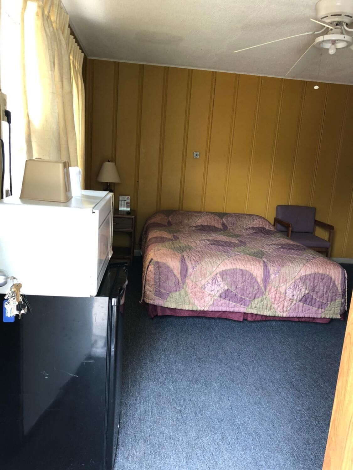 Ein Hotelzimmer mit einem Bett, einem Schreibtisch, einer Lampe und einem Deckenventilator.