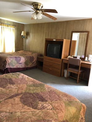 A hotel room with two beds, a desk with a chair, a television, a ceiling fan, and a mirror. - Coronado West Motel (Lindsborg)