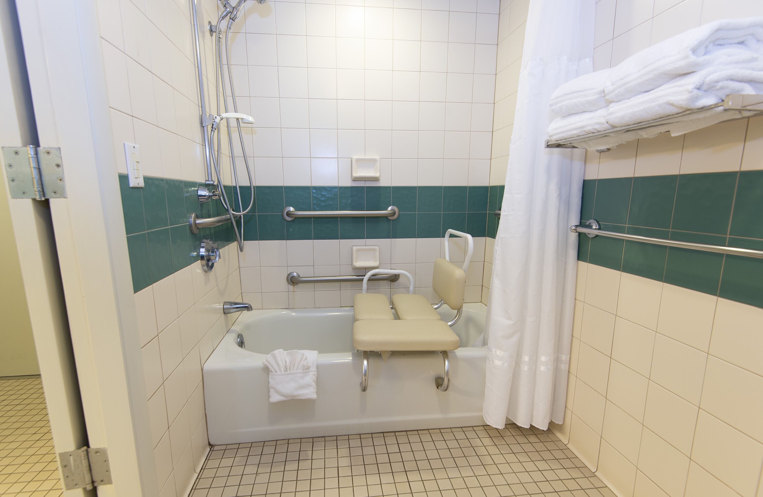 A bathroom with a bathtub, grab bars, a showerhead, and a towel rack.