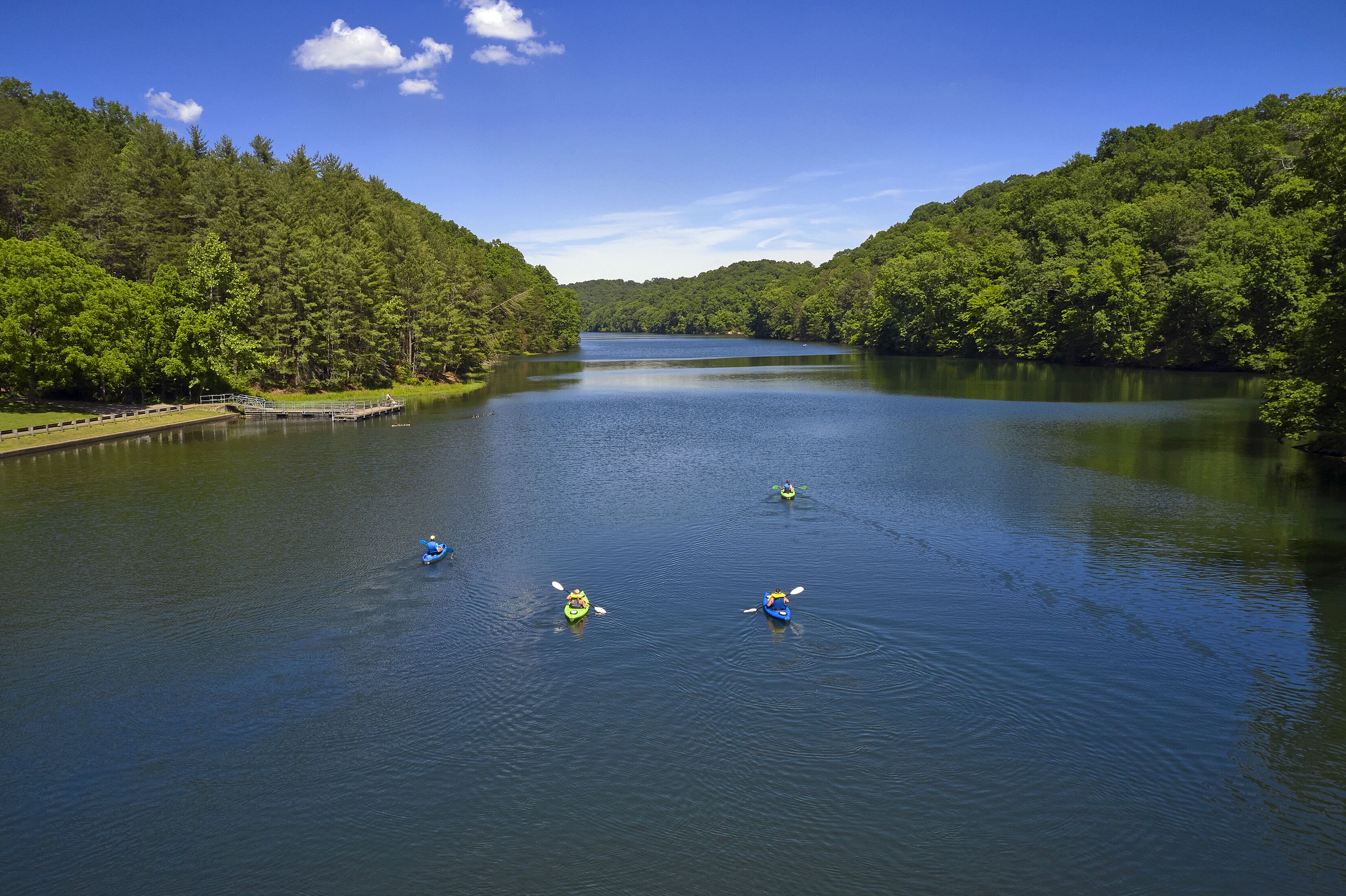 A calm lake surrounded by dense forest, with kayaks on the water.