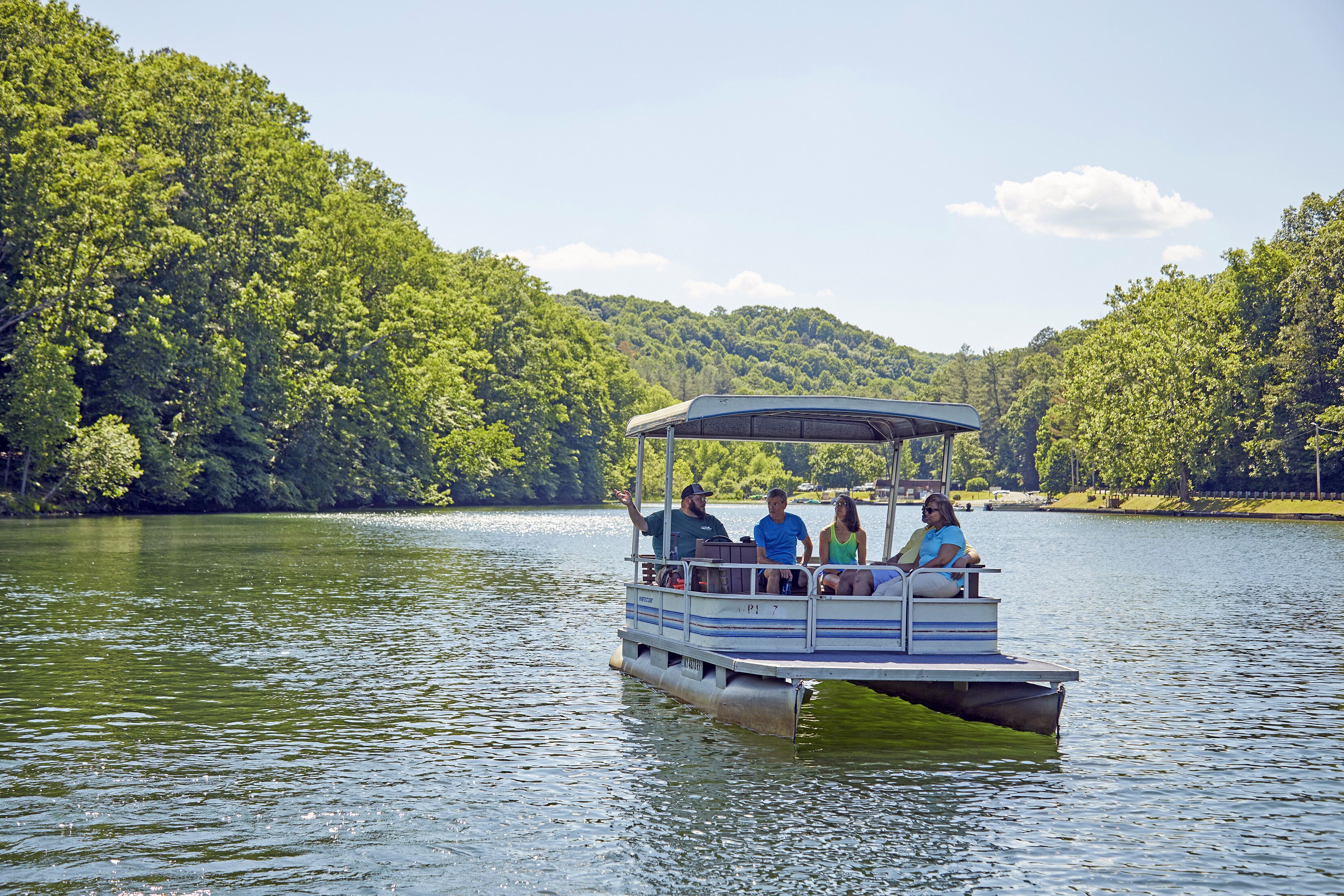 A boat with passengers on a calm lake surrounded by dense forest.