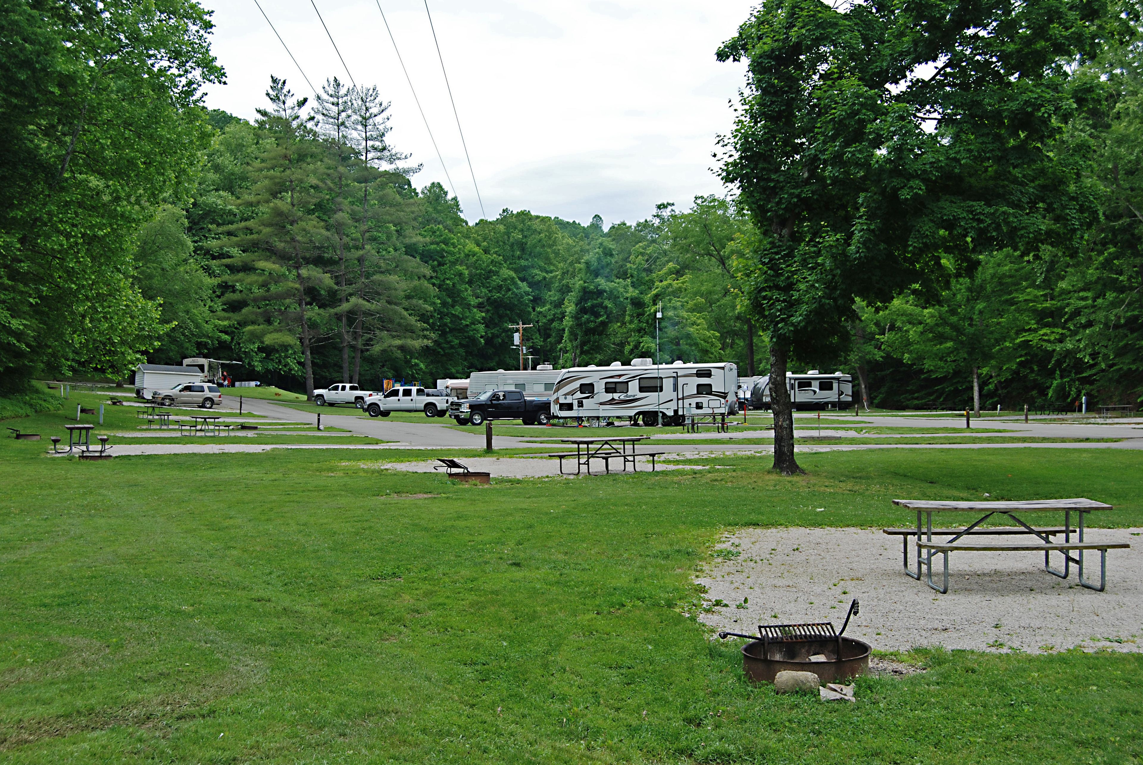 Un camping con vehículos recreativos estacionados, mesas de picnic y zona de barbacoa.