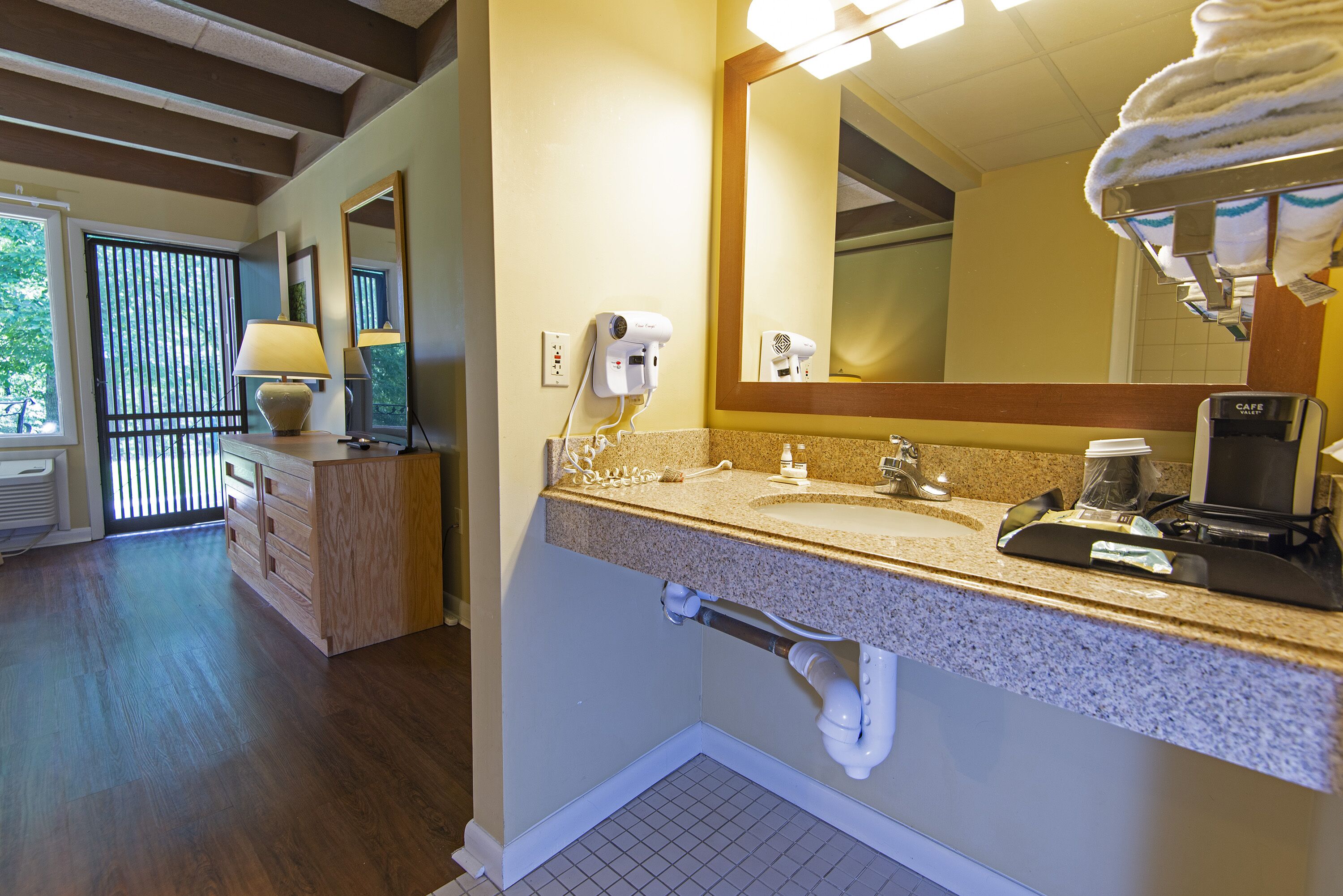 A bathroom with a sink, mirror, towel rack, and a coffee machine.