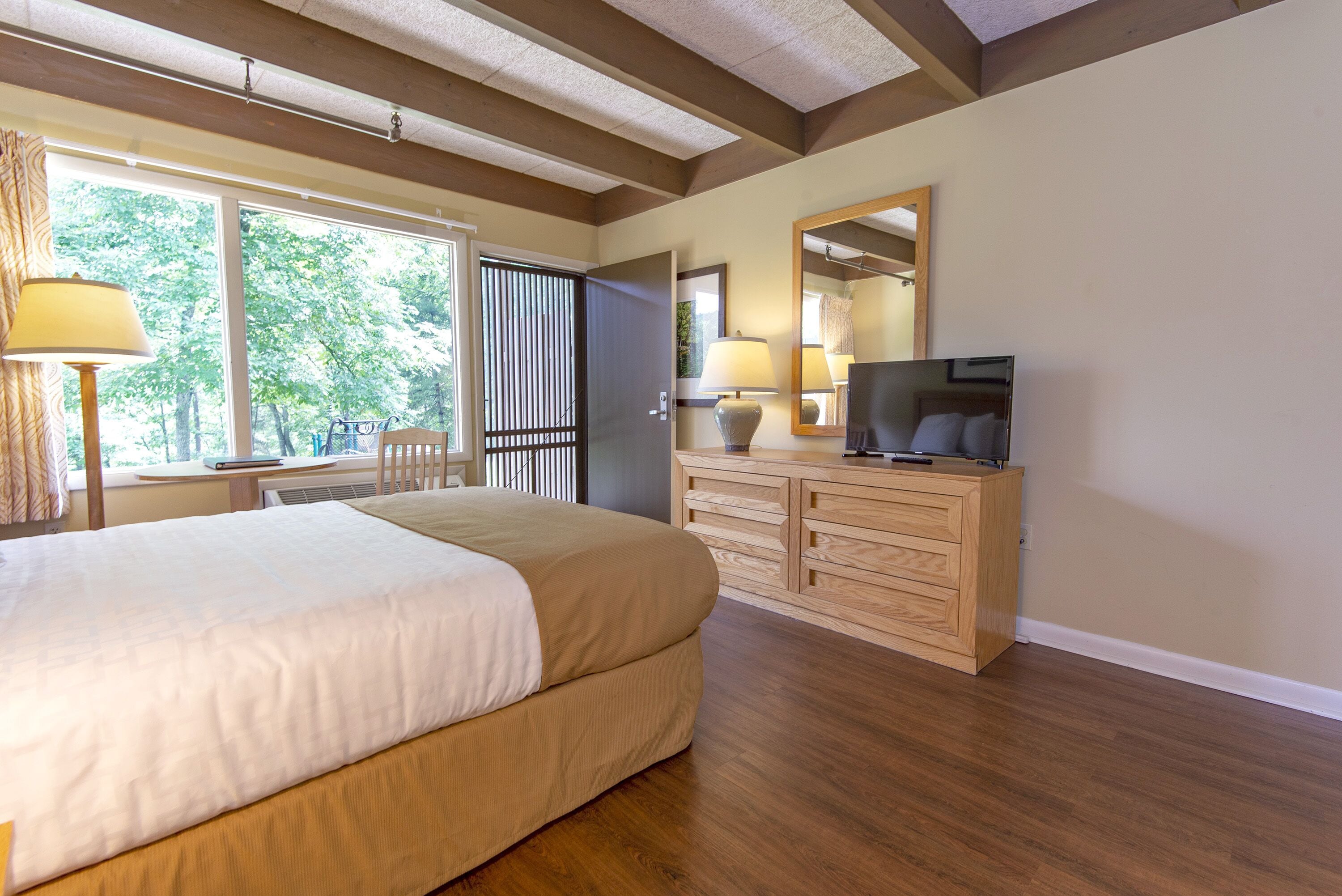 A bedroom with a large bed, wooden dresser, TV, and a window with blinds.