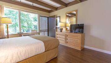 A bedroom with a large bed, wooden dresser, TV, and a window with blinds.