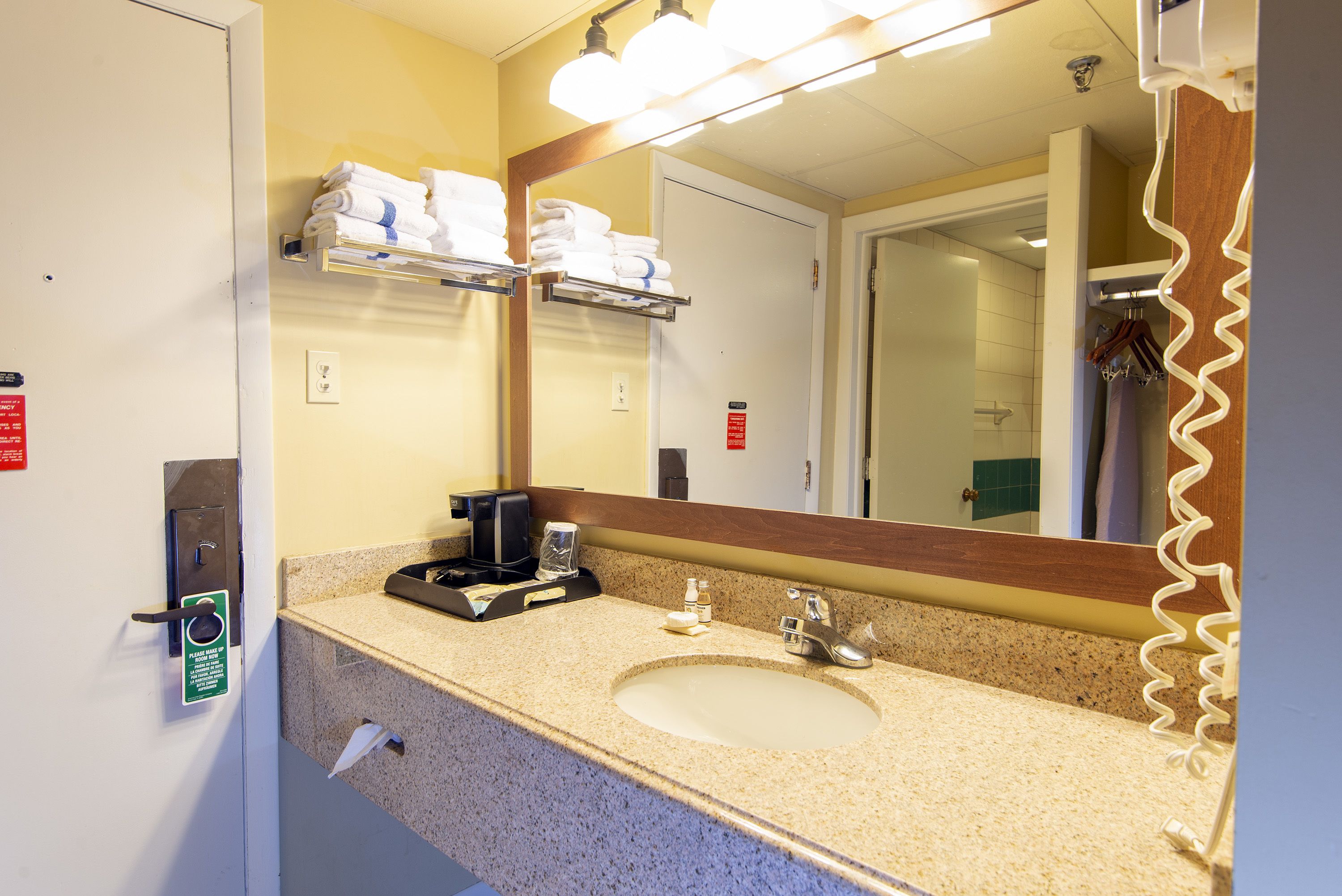 A hotel bathroom with a sink, mirror, towel rack, and a coffee maker.