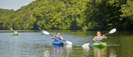 Trois personnes pratiquant le kayak sur un lac paisible, entouré d’une forêt dense.
