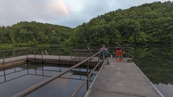 A concrete pier extending into a calm lake with a forested hill in the background.