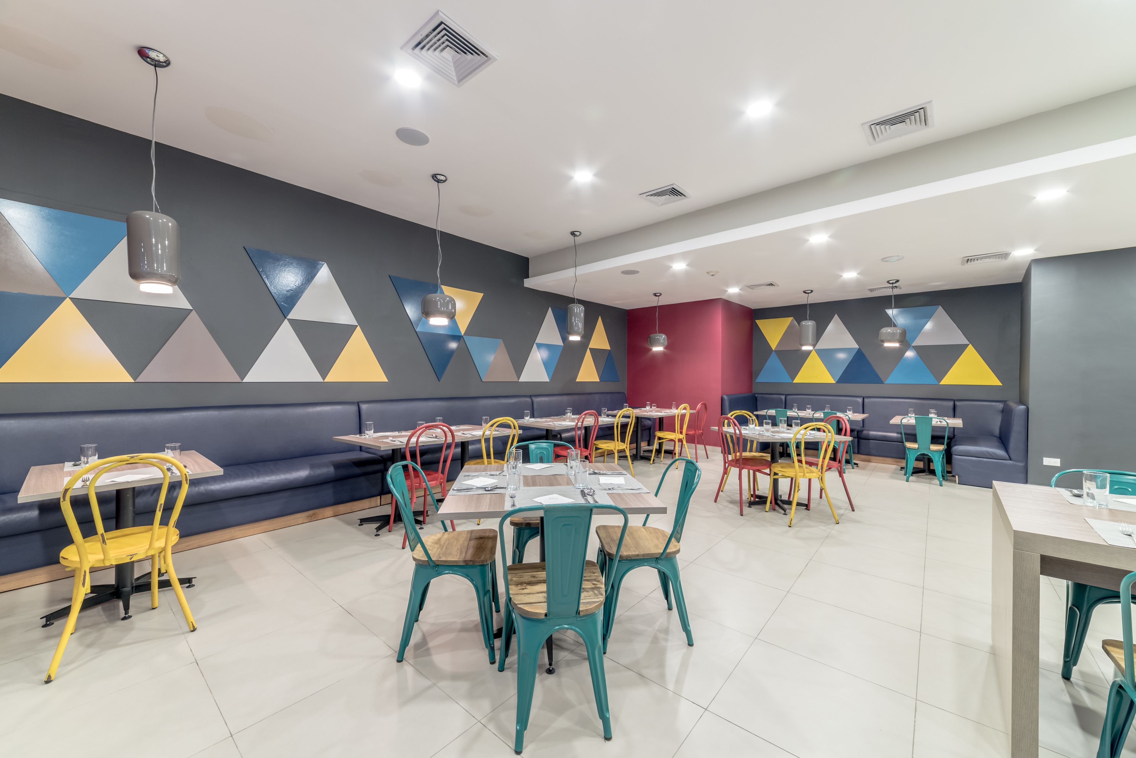 Ein modernes Restaurant mit Sitzecken und Tischen, bunter geometrischer Wandgestaltung und verschiedenen Stuhlfärben.