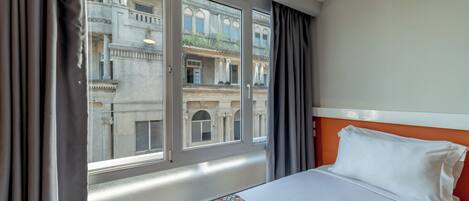 Une chambre d’hôtel avec un lit, une fenêtre avec des rideaux et une vue sur un immeuble.