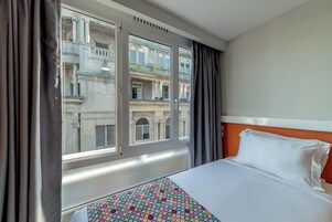 Una habitación de hotel con cama, ventana con cortinas y vista a un edificio.