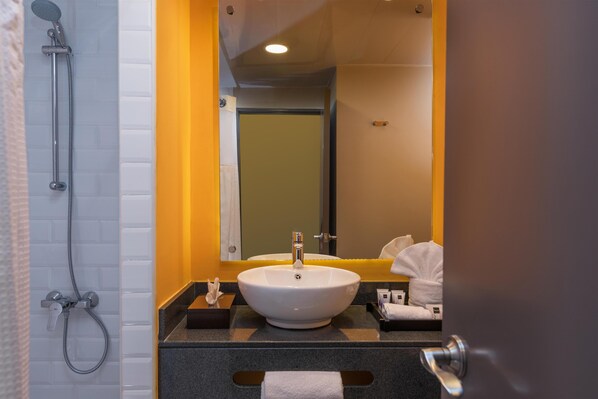 Un baño con un lavabo blanco, un cabezal de ducha de mano y un espejo con una pared de acento amarilla.