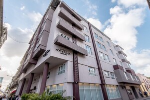 Un hotel de varios pisos con balcones, una entrada destacada y cielo despejado.