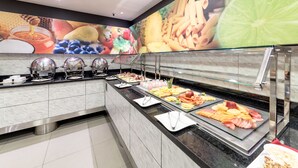 Un buffet proposant une variété de plats et une grande fresque murale représentant des fruits et des légumes.