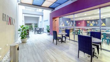 A modern indoor dining area with tables and chairs, a trash bin, and potted plants.