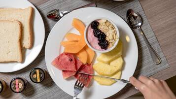A breakfast plate with toast, melon, pineapple, watermelon, and a bowl of yogurt with nuts and dried fruit.