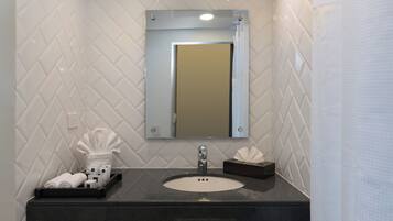 Une salle de bain avec un mur recouvert de carreaux blancs disposés en motif chevron, un plan de toilette noir, un lavabo rond, un miroir et un porte-serviettes.