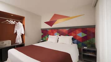 Ein Hotelzimmer mit einem großen Bett, einem Wandhaken für Bademäntel, einem Nachttisch mit Lampe und einem farbenfrohen geometrischen Wandmuster.